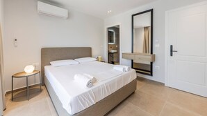 Habitación de hotel moderna con una cama grande, una mesita de noche, un espejo y un baño visible a través de una puerta abierta.