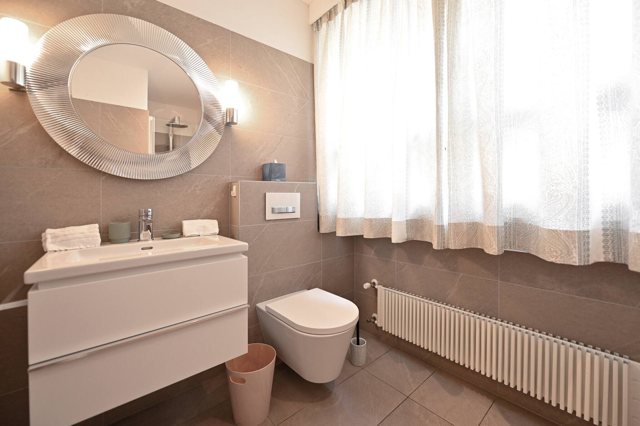 A modern bathroom with a round mirror, a toilet, a sink with a vanity, and a radiator.