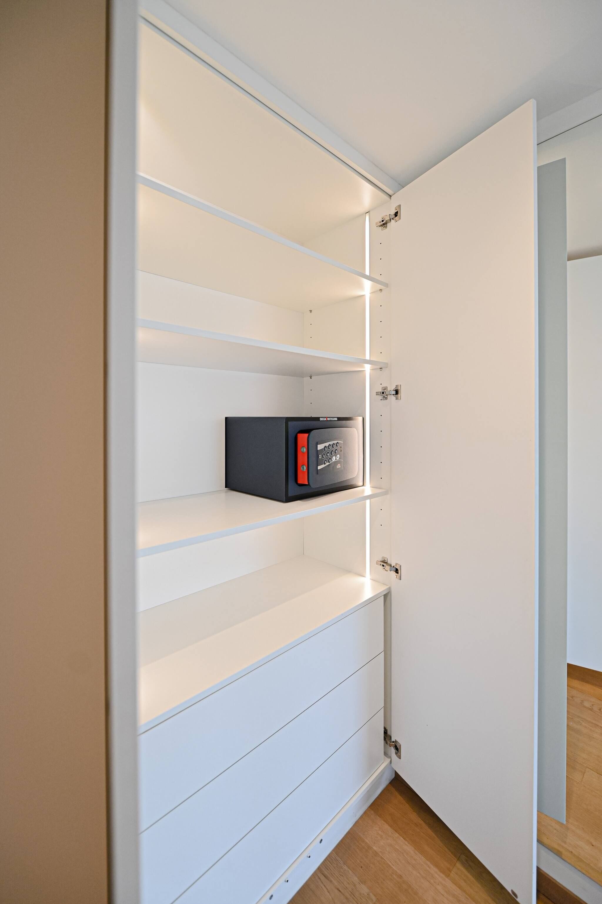 A white cabinet with multiple shelves, one of which contains a black electronic device.