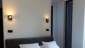 Une chambre moderne avec un grand lit, deux lampes fixées au mur et une fenêtre avec des stores.