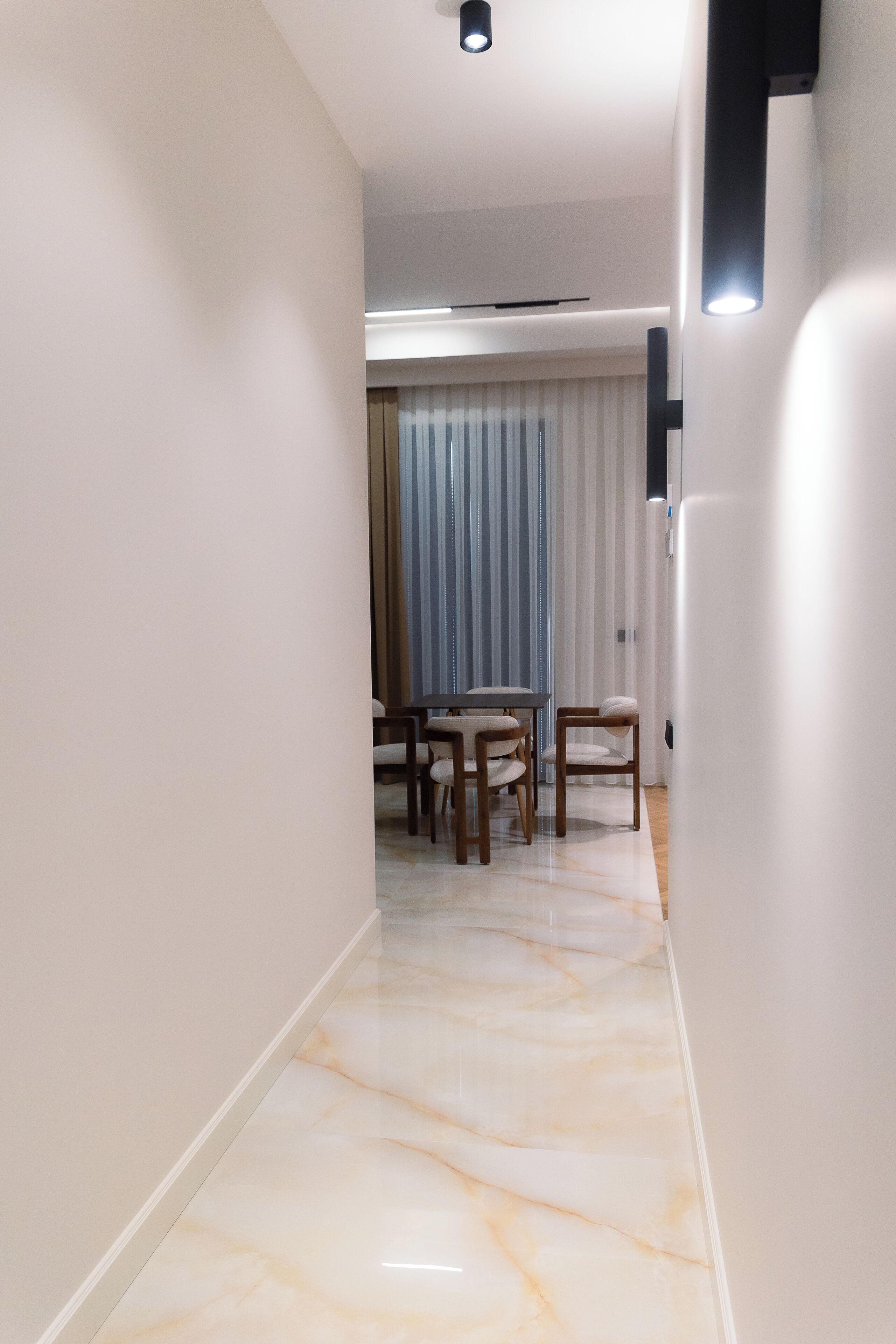 A hallway with a marble floor leading to a dining area with a table and chairs.