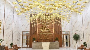 Eine Hotellobby mit einem Marmor-Rezeptionsschalter, einem großen Schild mit der Zahl '2' und einer Decke mit goldenen Anhängerdekorationen.