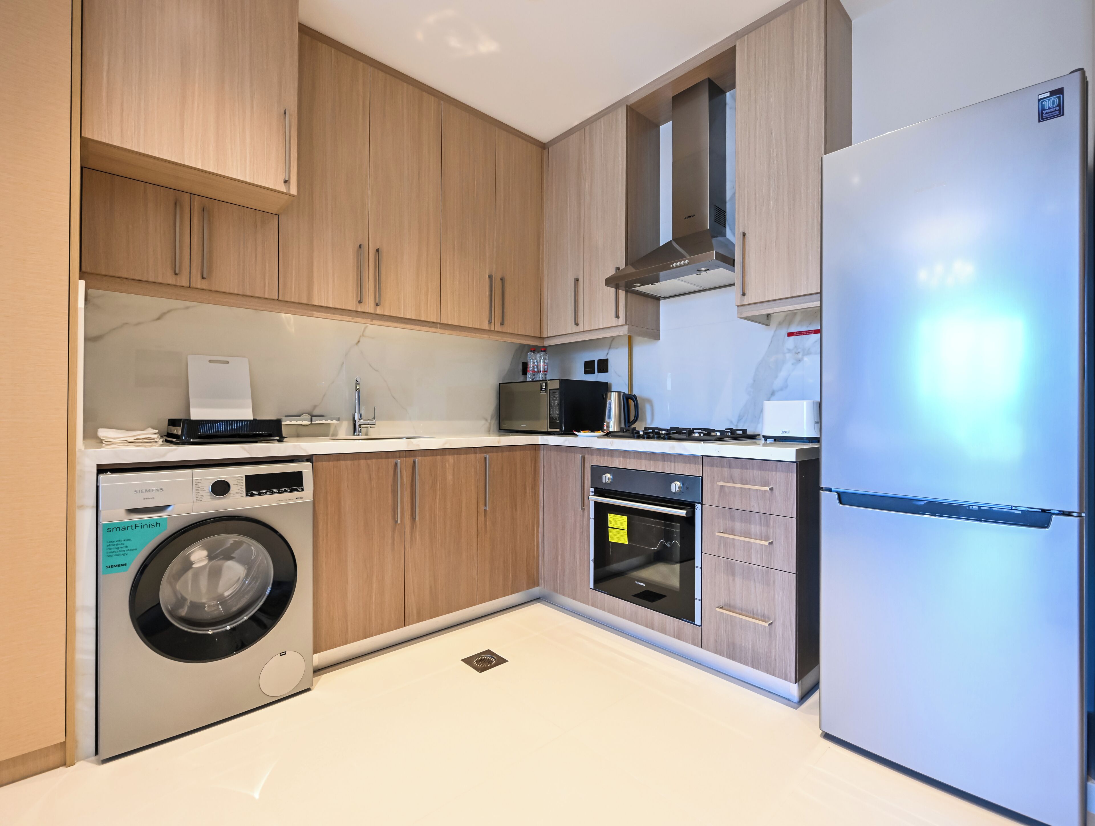 A modern kitchen with wooden cabinets, a built-in washing machine, a microwave, a stove, and a refrigerator.