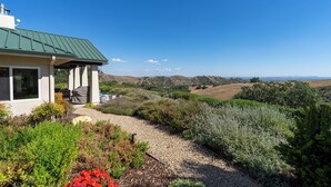 A house with a green roof, a patio with outdoor furniture, and a gravel path leading to a hilly landscape. - 40 Acres + Home Office + Views | Paso Robles | Skyeranch-30 Day Rental (San Miguel)