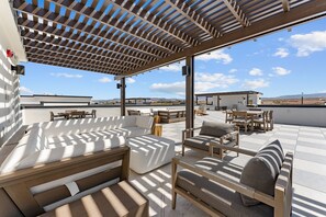 Eine Dachterrasse mit Sitzgelegenheiten im Freien, darunter Sofas und Stühle, die von einer Pergola beschattet werden.