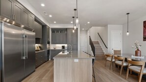 A modern kitchen with stainless steel appliances, a central island, and a dining area with wooden chairs.