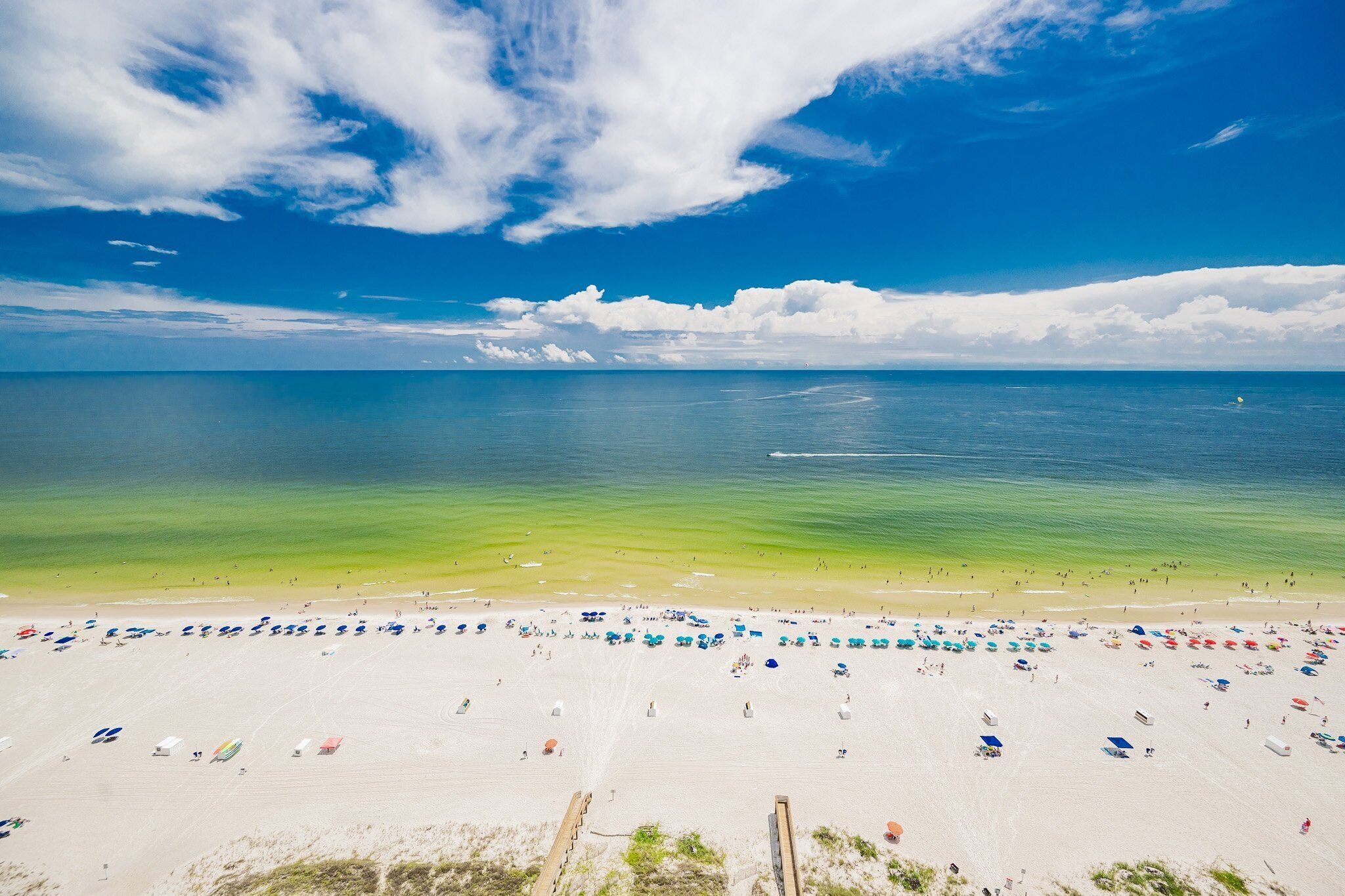 A beach with clear blue water, a sandy shore, and numerous umbrellas.