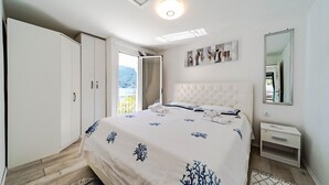 A bedroom with a bed, a wardrobe, a nightstand, a mirror, and a view of the outdoors.