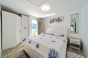 A bedroom with a bed, a wardrobe, a nightstand, a mirror, and a view of the outdoors.