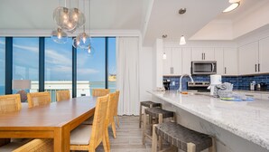 A modern kitchen with white cabinets, a microwave, and a large island with stools. - Phoenix Gulf Shores Ii 2001 4 Bedroom Condo (Gulf Shores)