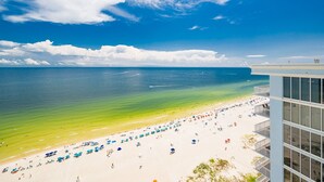 A beach with clear waters and a building with large windows overlooking the beach. - Phoenix Gulf Shores Ii 2001 4 Bedroom Condo (Gulf Shores)