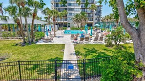 A pool area with lounge chairs and umbrellas, surrounded by palm trees and a building in the background. - Siesta Beach Retreat 2 Bedroom Townhouse (Siesta Key)