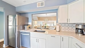 A modern kitchen with a stainless steel refrigerator, a built-in dishwasher, white cabinets, and a coffee maker. - Siesta Beach Retreat 2 Bedroom Townhouse (Siesta Key)