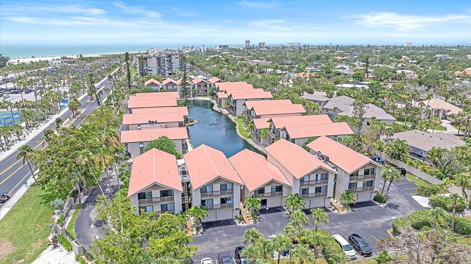 A coastal resort with multiple buildings featuring red roofs, a central water body, and a view of the beach and ocean.