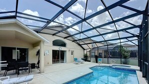 Una piscina interior con agua cristalina y azul, rodeada por un porche cubierto con sillones de descanso y una estructura de vidrio.