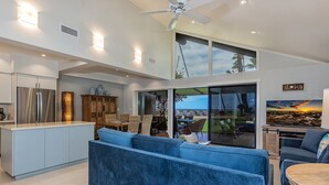 A modern kitchen with a built-in island, a blue sofa, and a dining area with wicker chairs. - Maalaea Surf B1 2 Bedroom Condo (Kihei)