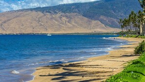 A beach with a clear view of the ocean, a distant mountain range, and a few wind turbines. - Maalaea Surf B1 2 Bedroom Condo (Kihei)