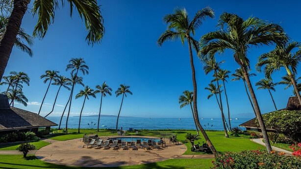 A pool area with lounge chairs, surrounded by palm trees and a view of the ocean. - Maalaea Surf B1 2 Bedroom Condo (Kihei)