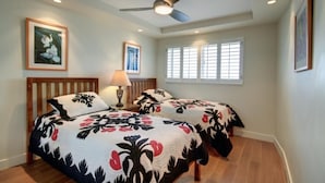 A bedroom with two beds, a ceiling fan, a window with blinds, and framed artwork on the walls. - Menehune Shores, #510^ 3 Bedroom Condo (Kihei)