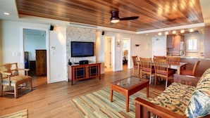 A spacious living area with a wooden ceiling, a flat-screen TV, a dining table with chairs, and a sofa. - Menehune Shores, #510^ 3 Bedroom Condo (Kihei)