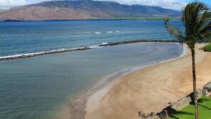 A beach with clear water, a stone wall, and a mountain in the background. - Menehune Shores, #510^ 3 Bedroom Condo (Kihei)