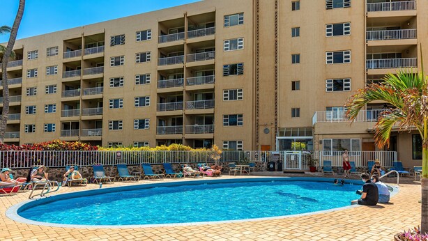 A hotel with a swimming pool surrounded by lounge chairs and a palm tree. - Menehune Shores, #510^ 3 Bedroom Condo (Kihei)