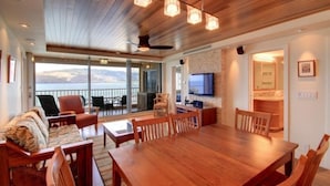 A spacious living area with a wooden dining table, comfortable seating, a flat-screen TV, and a balcony with a view. - Menehune Shores, #510^ 3 Bedroom Condo (Kihei)