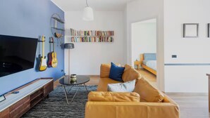 A modern living room with a large flat-screen TV, guitars, a bookshelf, a sofa, and a coffee table.