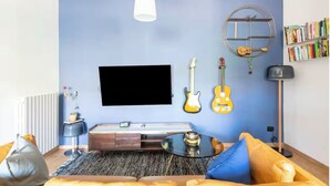 A modern living room with a flat-screen TV, a guitar, a bookshelf, and a round shelf with a guitar hanging on it.