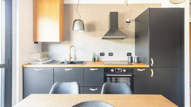 A modern kitchen with a wooden table, black cabinets, a built-in oven, and a hexagonal backsplash.
