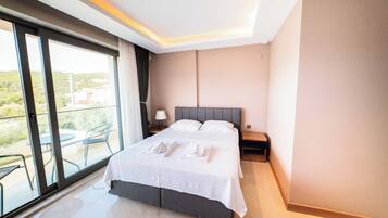 A modern hotel room with a large bed, a nightstand, a lamp, and a view of the outdoors through a sliding glass door.