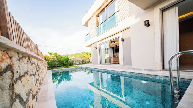 A modern two-story house with a swimming pool, a stone wall, and a glass door leading to the interior. - Villa Meyra (Kas)