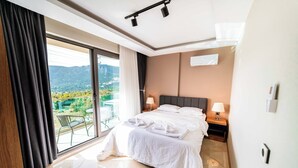 A hotel room with a bed, two bedside lamps, a nightstand, a large window with curtains, and a view of greenery and mountains. - Villa Meyra (Kas)
