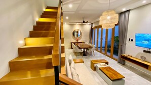 Un intérieur moderne avec un escalier en bois, un coin repas agrémenté d’un grand miroir rond et un grand téléviseur fixé au mur.