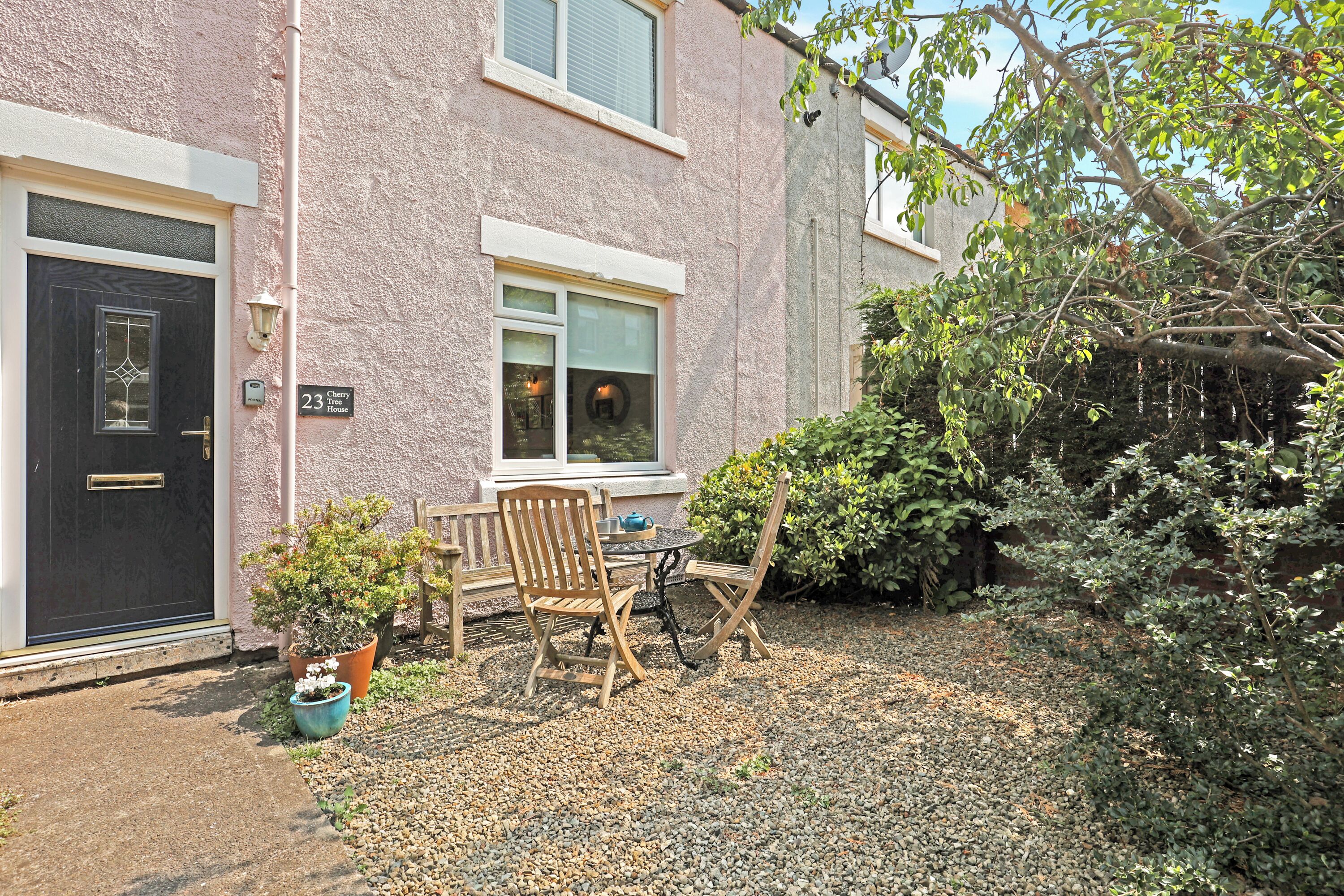 A two-story building with a black door and windows. There is a small patio area with a table and chairs, and a potted plant.