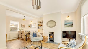 A cozy living room with a fireplace, a dining area, and a TV. - Cherry Tree House - North East Escapes (Amble)