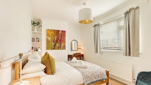 A neatly arranged bedroom with a wooden bed, bedside table, lamp, and a window with curtains. - Cherry Tree House - North East Escapes (Amble)