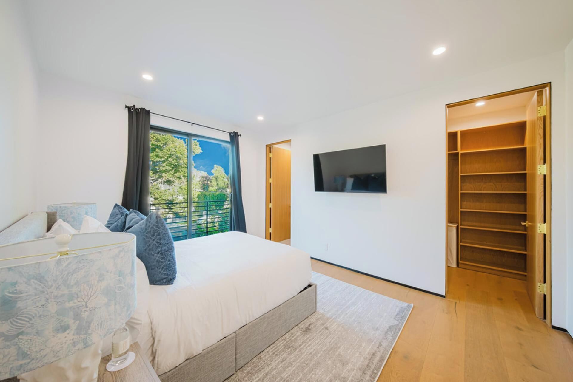 A bedroom with a bed, a TV, a wardrobe, and a window with a view of trees.
