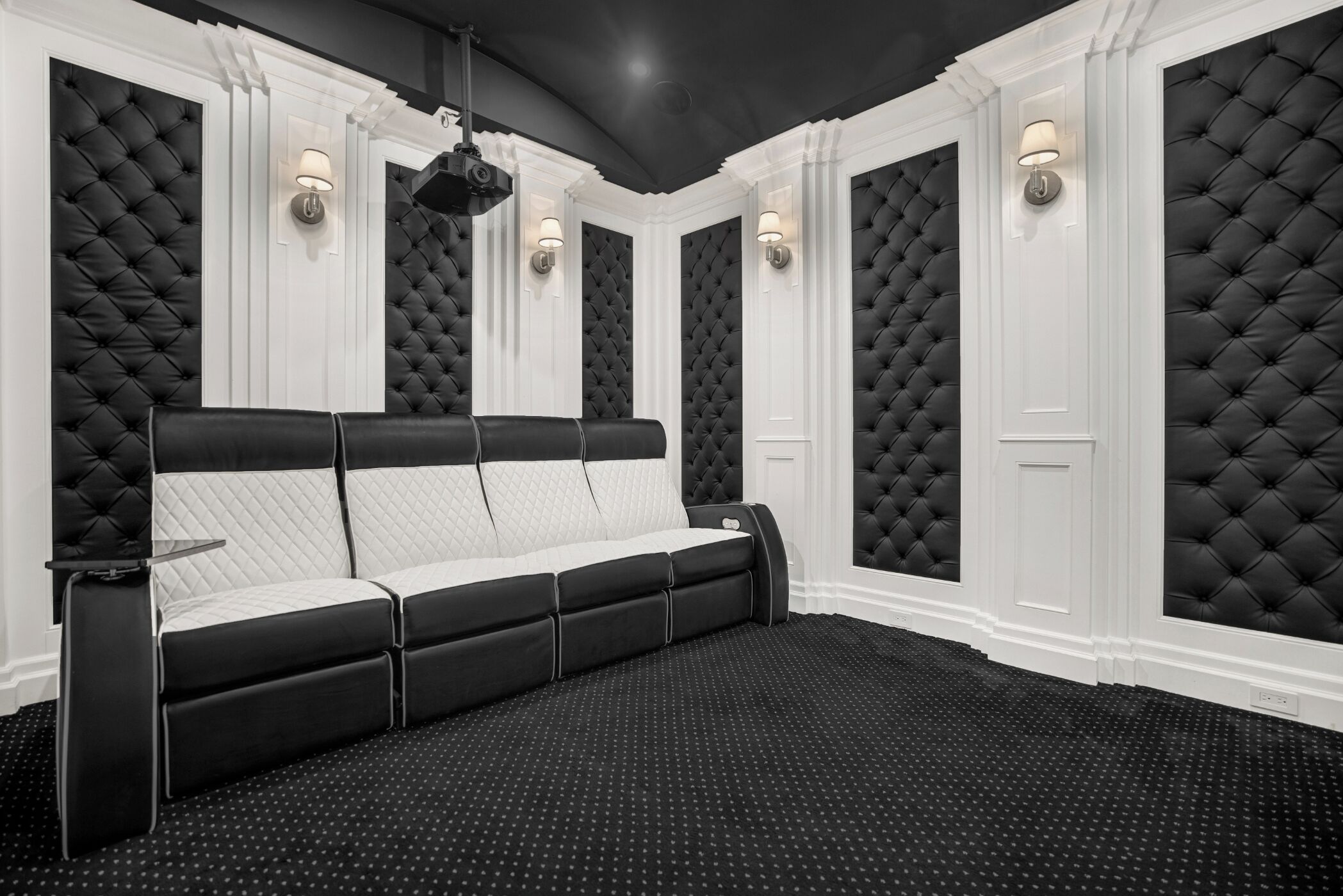 A black and white room with a tufted headboard sofa, wall sconces, and a polka dot carpet.