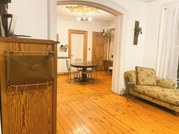 A living room with a wooden floor, a dining table with chairs, a sofa, and a decorative mirror.