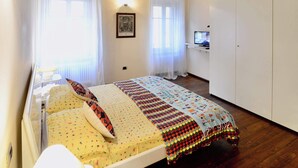 Une chambre avec un plafond en bois, un lit recouvert d’une courtepointe colorée, une table de chevet avec une lampe et un téléviseur posé sur une étagère.