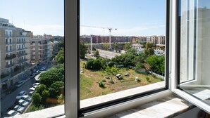 A view from a window overlooking a cityscape with buildings, a construction site, and a road with parked cars. - Gil s Penthouse by Wonderful Italy (Bari)