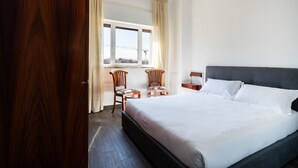 A hotel room with a large bed, two chairs, a window with curtains, and a wooden door. - Gil s Penthouse by Wonderful Italy (Bari)