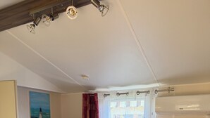 Una habitación acogedora con un sofá rojo, una mesita de madera, una ventana con cortinas y un cuadro de un faro.