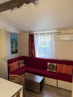 Una habitación acogedora con un sofá rojo, una mesita de madera, una ventana con cortinas y un cuadro de un faro.