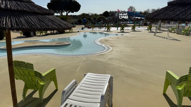 Un área de piscina con sillones de descanso y una estructura de techo de paja.
