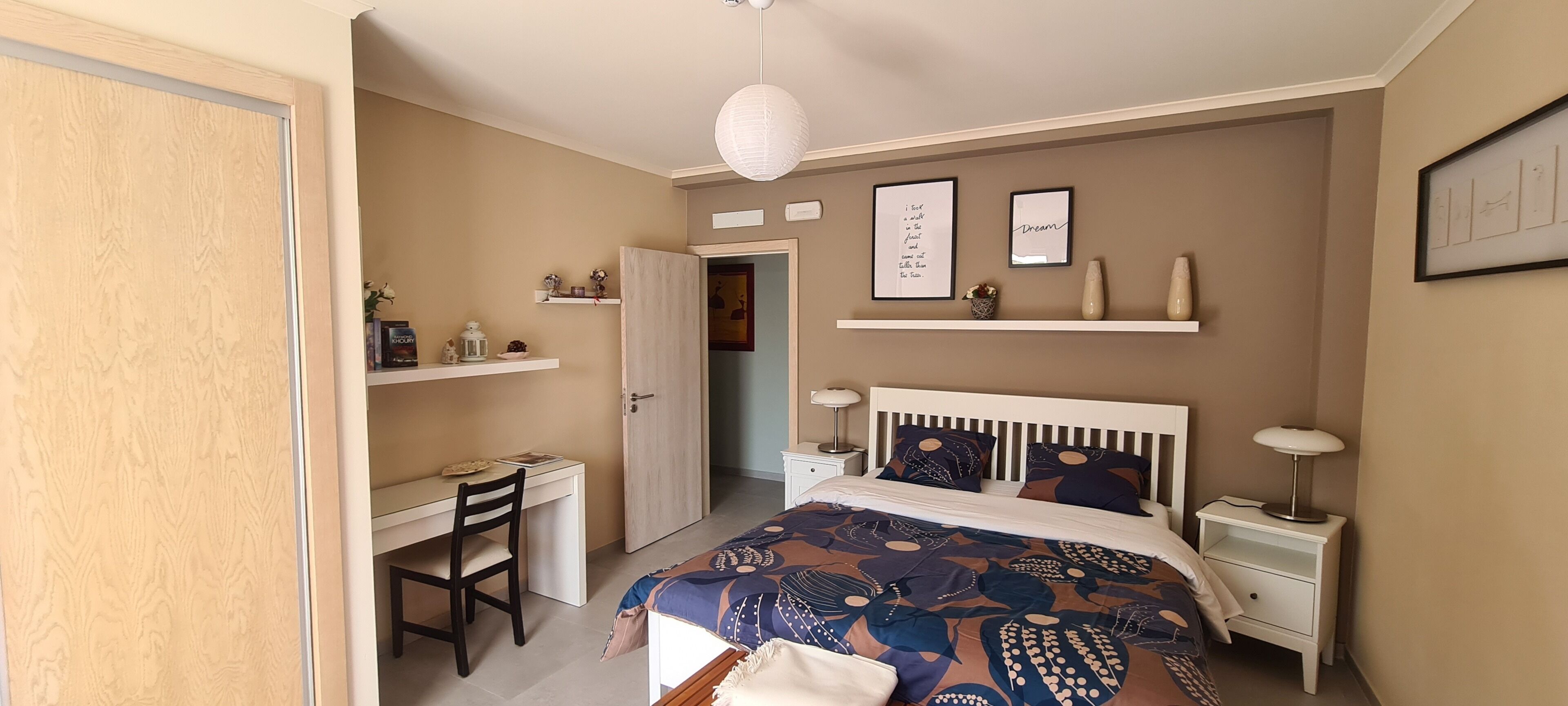 Ein Schlafzimmer mit Bett, Schreibtisch, Stuhl, Nachttischen und Regalen mit Dekoration.