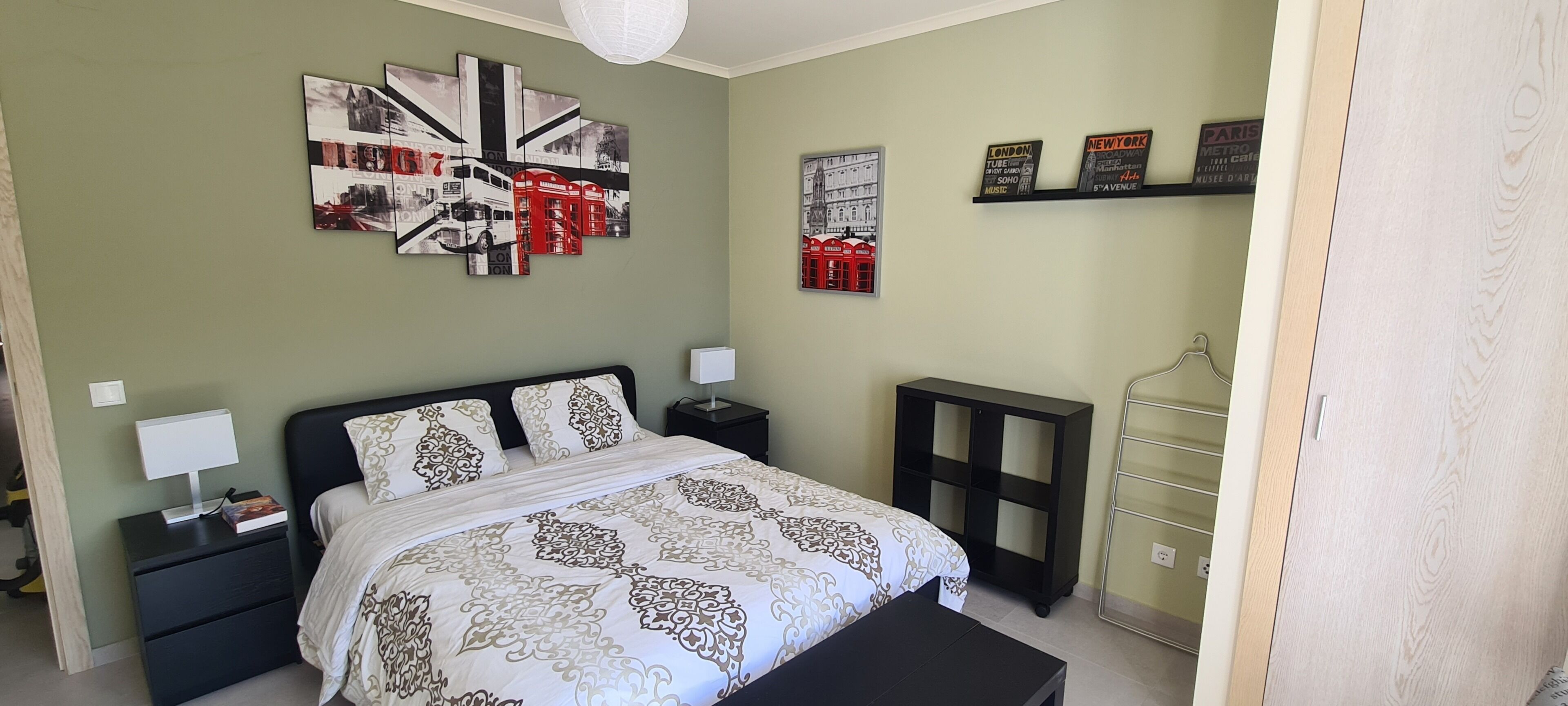 Ein Schlafzimmer mit Bett, Nachttischen, einem Kleiderschrank und einer Wand mit Kunstwerken.