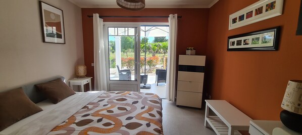 A bedroom with a bed, a desk, a wardrobe, and a balcony with a view of the outdoors.