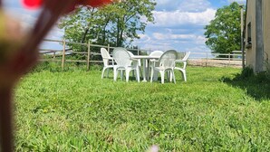 Un espace extérieur verdoyant avec une table et des chaises blanches, une clôture en bois et un bâtiment en arrière-plan.
